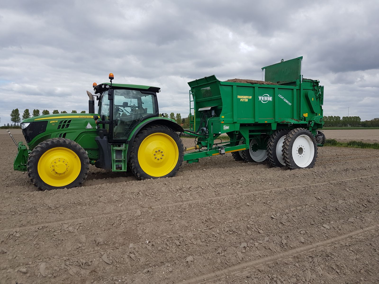 John Deere trekker met een groene mestverspreider op een kaal veld