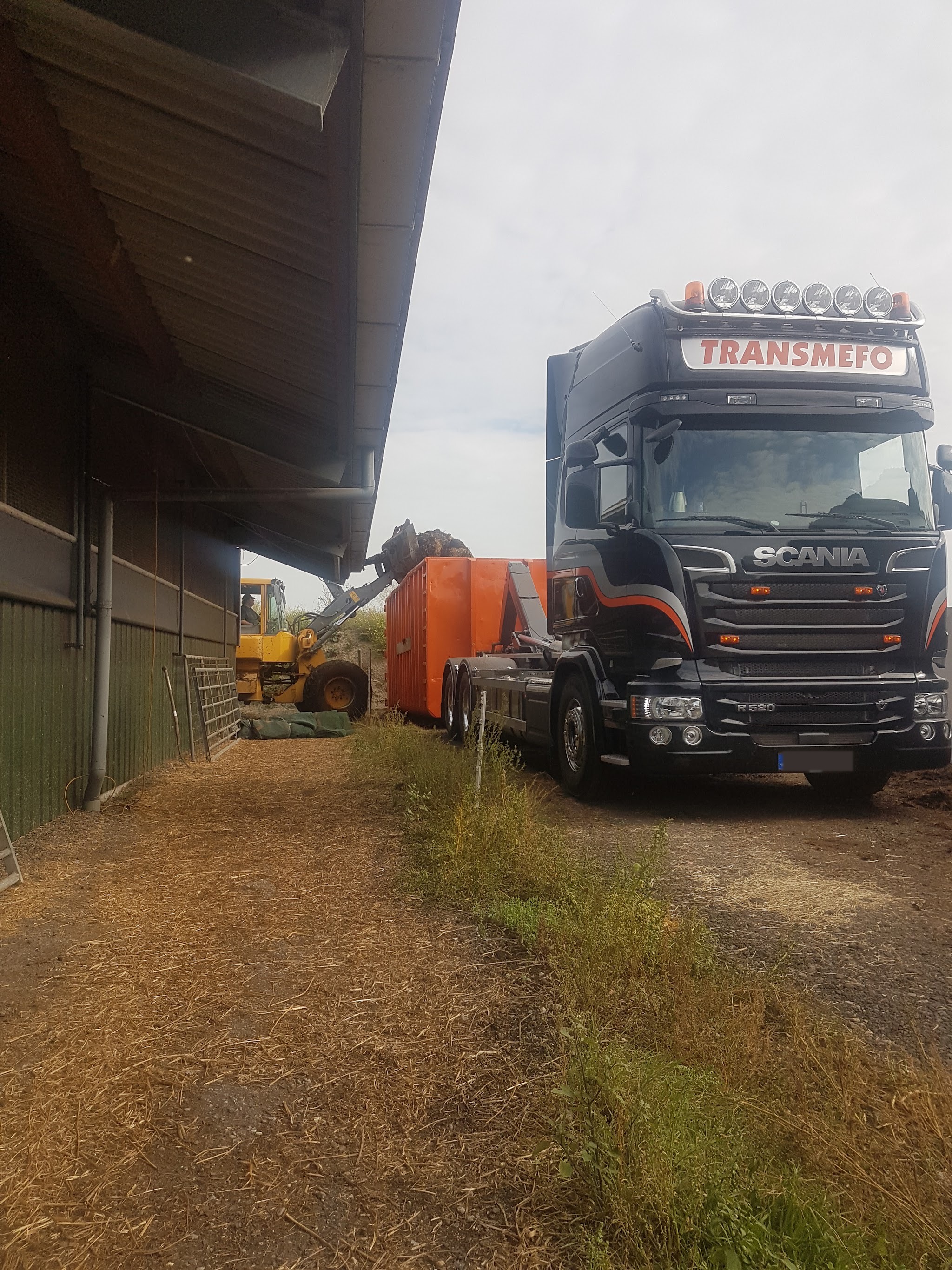 Scania TRANSMEFO naast een schuur, een shovel laadt de oranje container